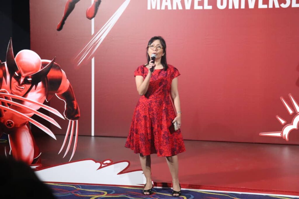 Rachel Nainggolan - Senior Brand Manager, CCA PNG wearing a red dress and holding a mic on a red stage at the Coca-Cola PNG premier of Deadpool.