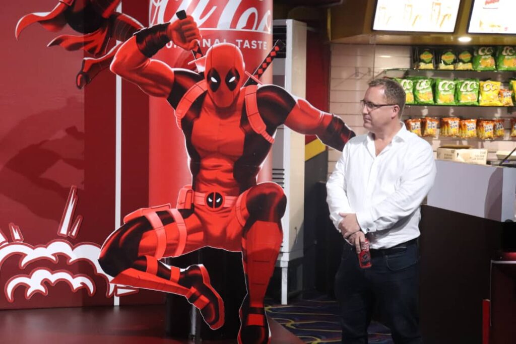 Tim Solly- Sales and Commercial Director, Coca-Cola PNG standing next to an image of Marvel Superhero, Deadpool.
