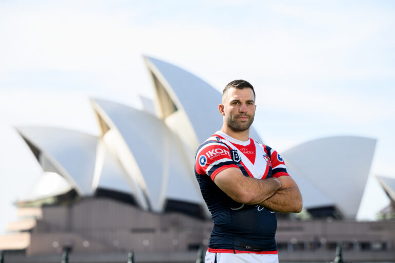James Tedesco wearing a Rooster Jersey standing with his arms crossed in front of the Sydney Opera House.
