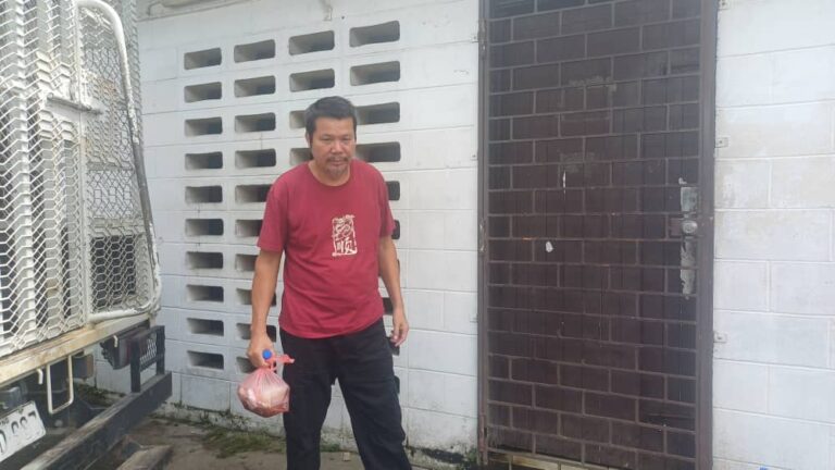 Transnational Crime Unveils: Chinese Mine Boss Sentenced by Lae’s Court Li Dezhang, a Chinese man wearing a red shirt and black pants standing in front of a brick building holding a small parcel.