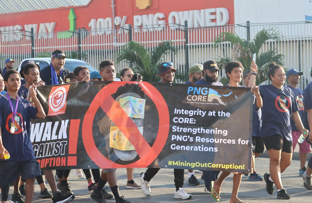 Men and women wearing blue shirts holding a banner during the walk of corruption