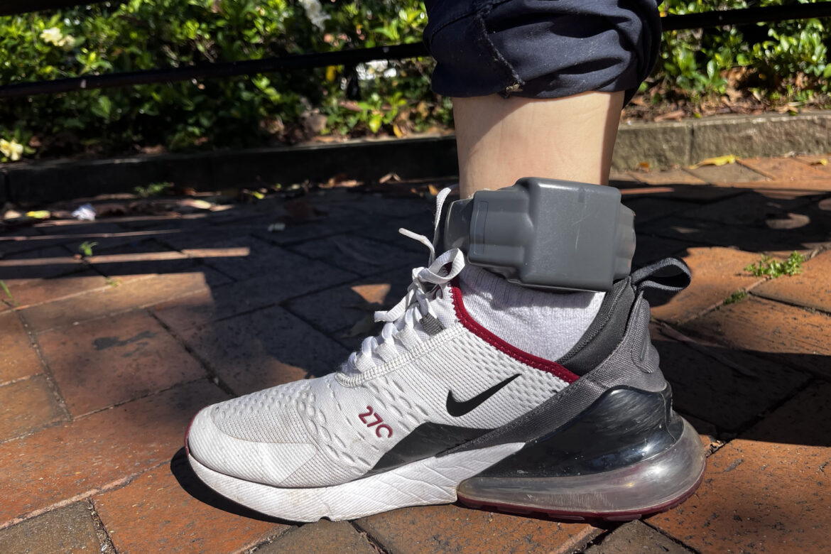 Ankle monitor strapped around a single leg wearing running shoes.
