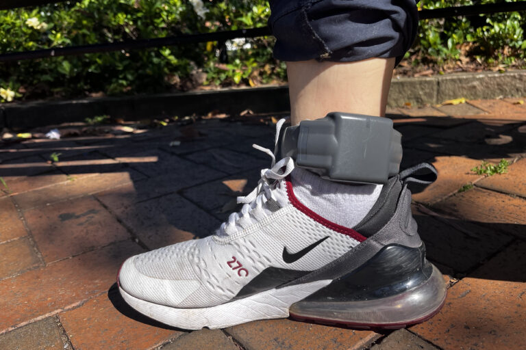 Ankle monitor strapped around a single leg wearing running shoes.