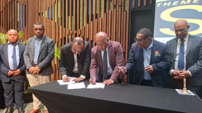 Guardian of the Public Purse: CPAPNG Launches Bold Reform to Secure District Finances Six men in suits, two bent over the table signing documents while standing up