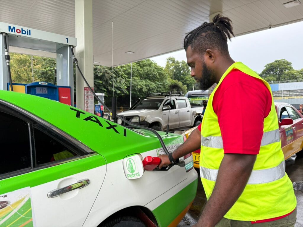 Darked skinned young man holding a fuel pump and putting petrol into a car.