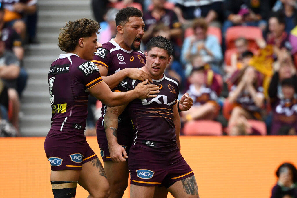 Three Brisbane Broncos male players getting into a huddle on the field of play