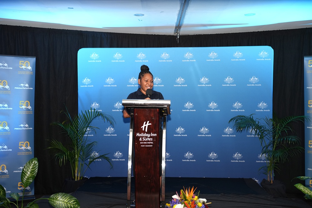 Dr Kalen Karapen standing at a podium on stage speaking.