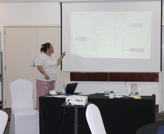 Woman wearing a white top and pink skirt making a powerpoint presentation at a whiteboard